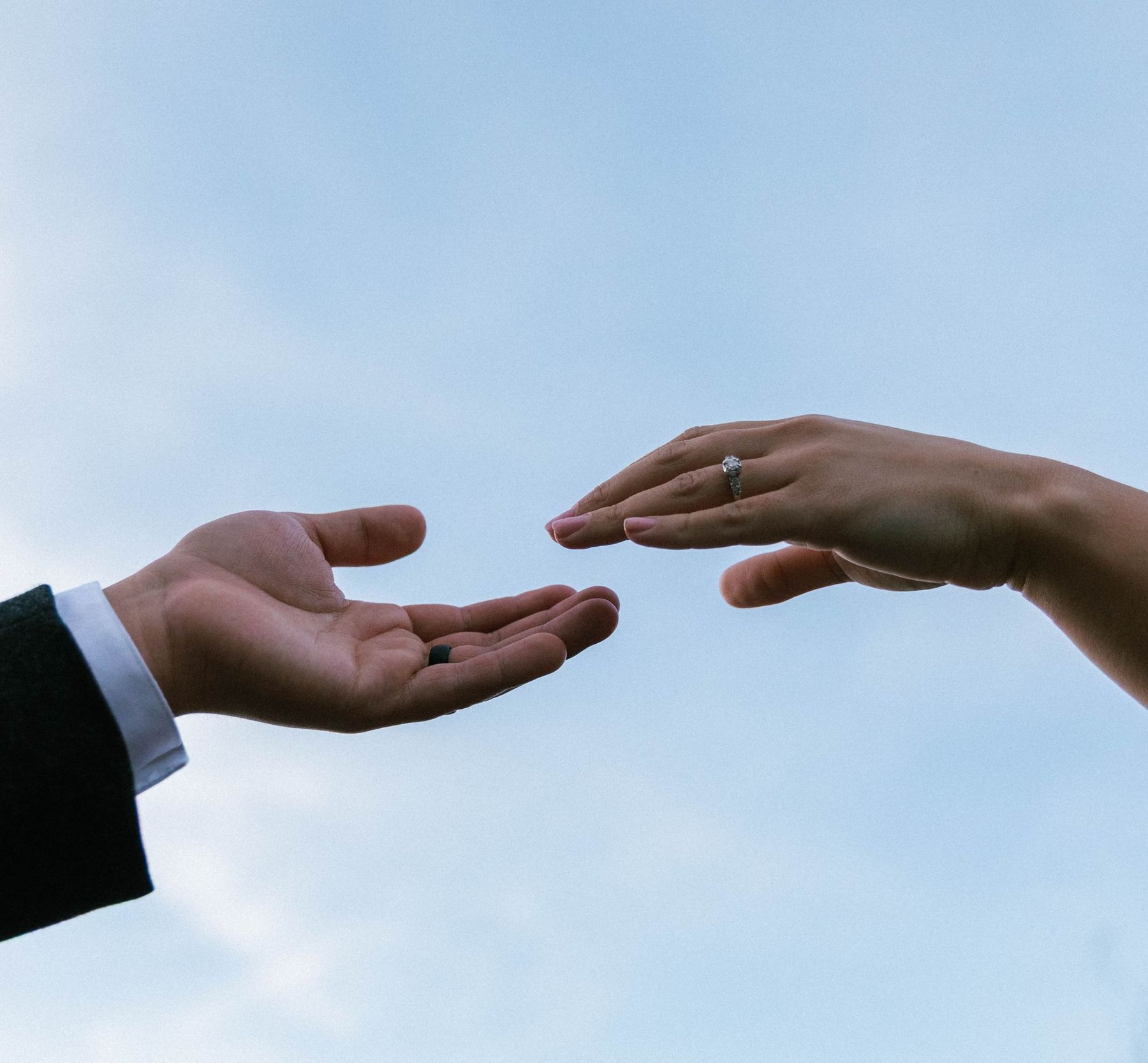 Two hands reaching toward each other, a ring catching the sky