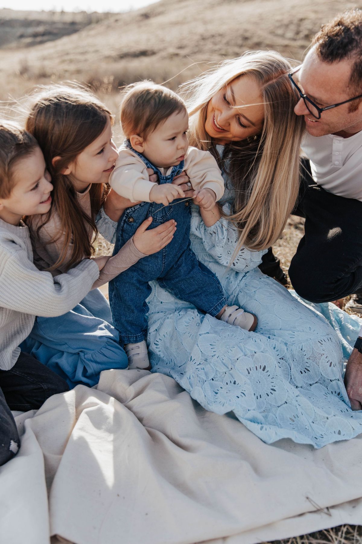 A family of five laughing together on a blanket in the field