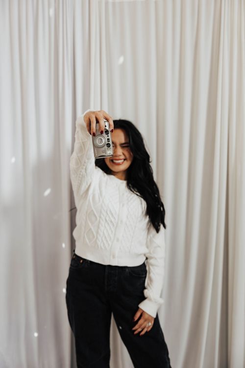 Lyka raising her film camera beside a soft curtain